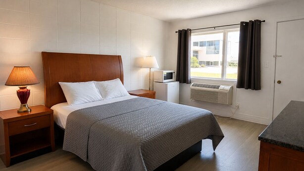 A neatly arranged hotel room with a bed, bedside lamps, a small table, and a window with curtains.
