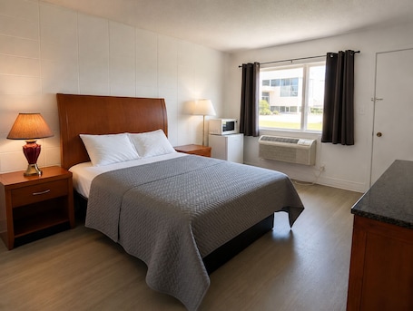 A neatly arranged hotel room with a bed, bedside lamps, a small table, and a window with curtains.. Huron Coast INN