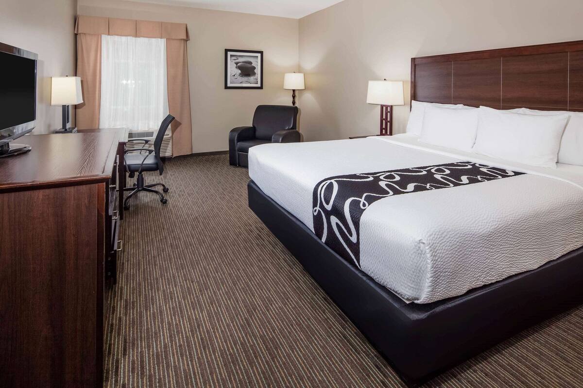 A hotel room with a large bed, a desk with a computer, two chairs, and a television.