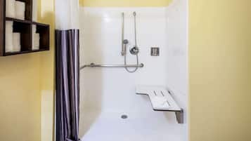 Zona de ducha con barra de apoyo, repisa con toallas y cabezal de ducha.