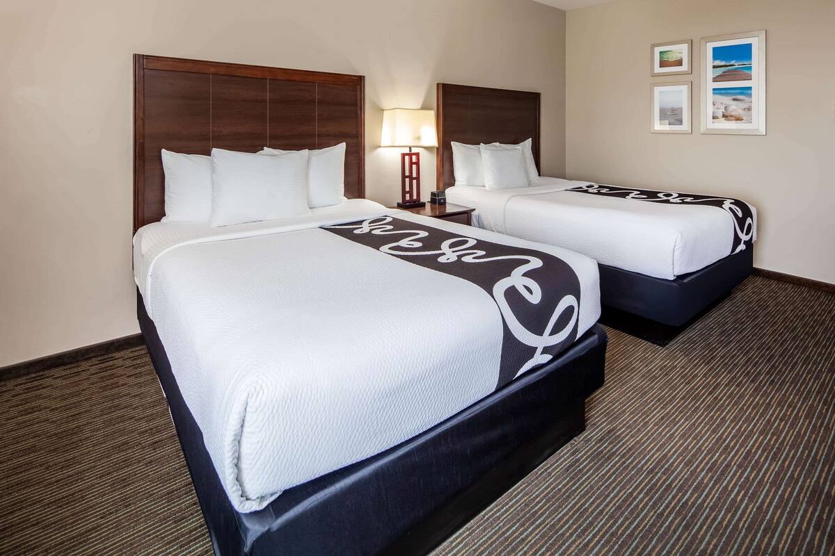 A hotel room with two beds, a nightstand with a lamp, and framed pictures on the wall.