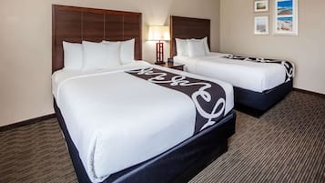 Habitación de hotel con dos camas, una mesita de noche con lámpara y cuadros en la pared.