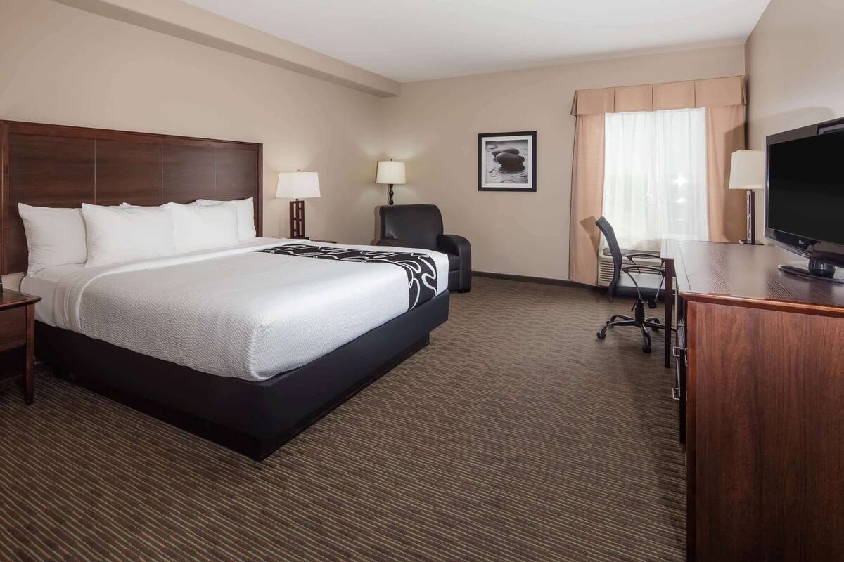 A hotel room with a large bed, a desk with a TV, a chair, and a lamp.