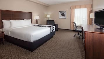 A hotel room with a large bed, a desk with a TV, a chair, and a lamp.