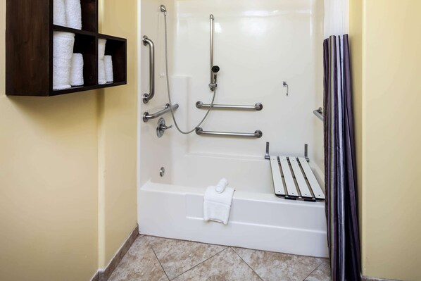 Une salle de bain équipée d’une baignoire, de barres d’appui, d’une étagère avec des serviettes et d’un rideau de douche.
