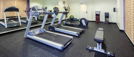 A gym with treadmills, an elliptical, a bench press, and a mirrored wall.