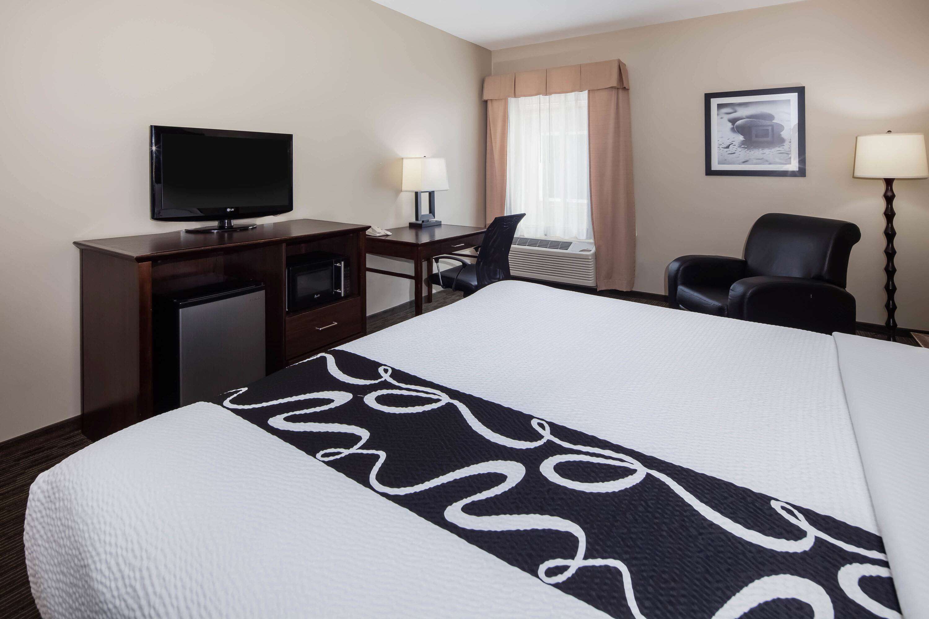 Habitación de hotel con cama, escritorio, televisor, silla y lámpara de escritorio.