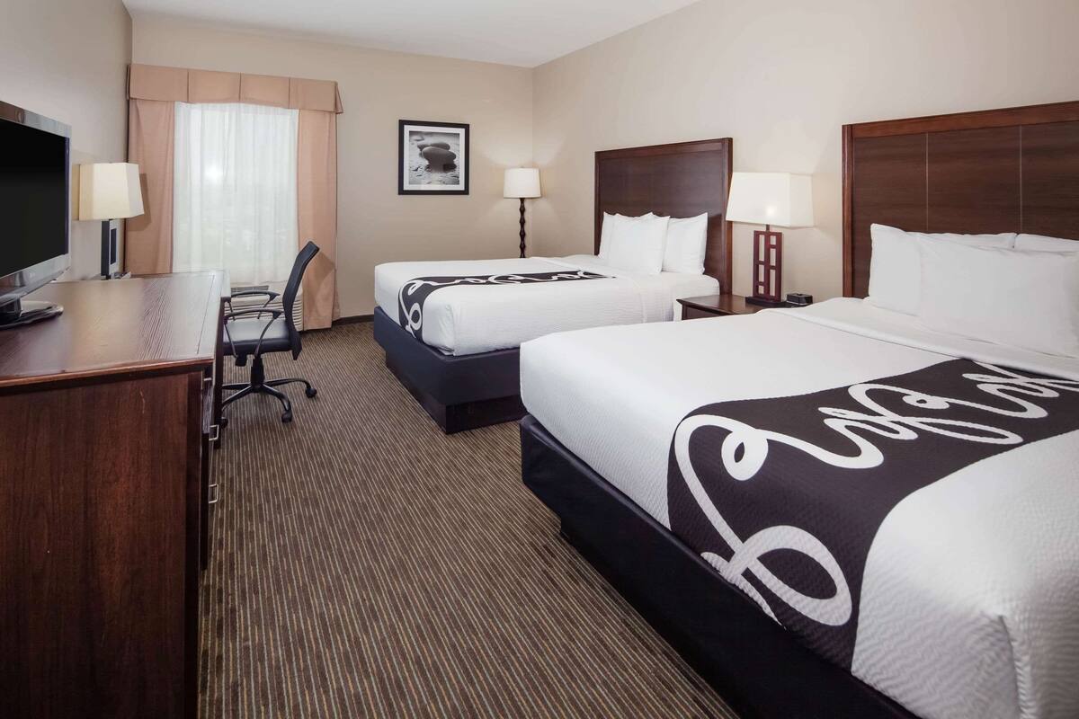 A hotel room with two beds, a desk with a TV, and a chair.