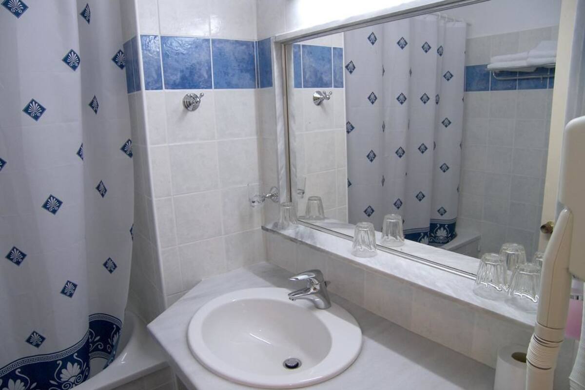 Une salle de bain avec un lavabo blanc, un miroir et un rideau de douche à motifs bleus.