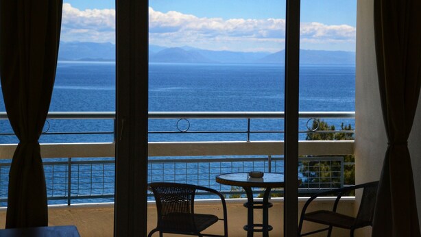 A balcony with a view of the ocean and mountains. There are two chairs and a table. - Alexandros Hotel -  All Inclusive (Corfu)