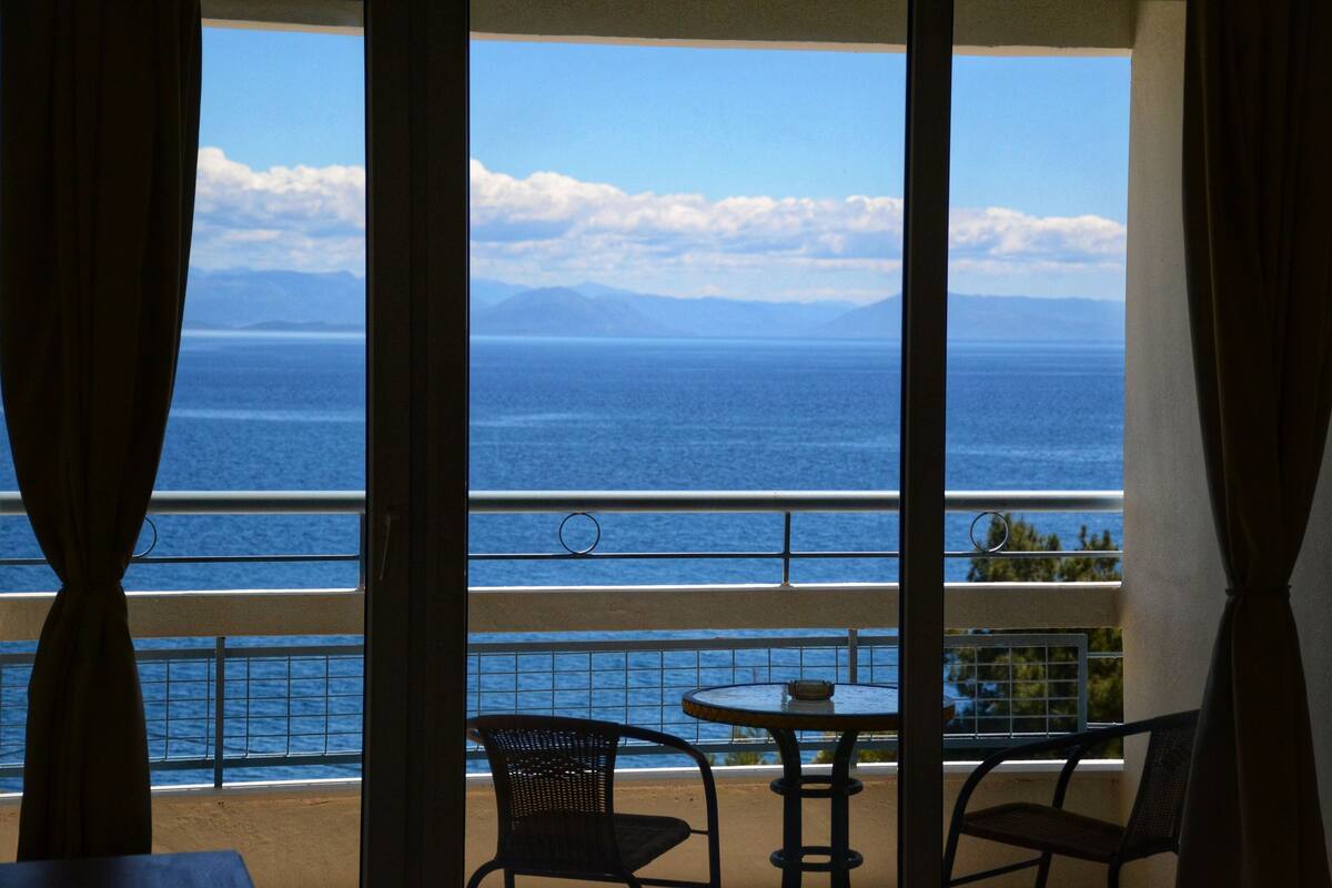 Un balcon avec vue sur l’océan et les montagnes. On y trouve deux chaises et une table.
