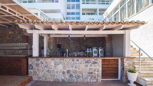 An outdoor bar area with a stone counter, wooden flooring, and a pergola overhead. - Alexandros Hotel -  All Inclusive (Corfu)