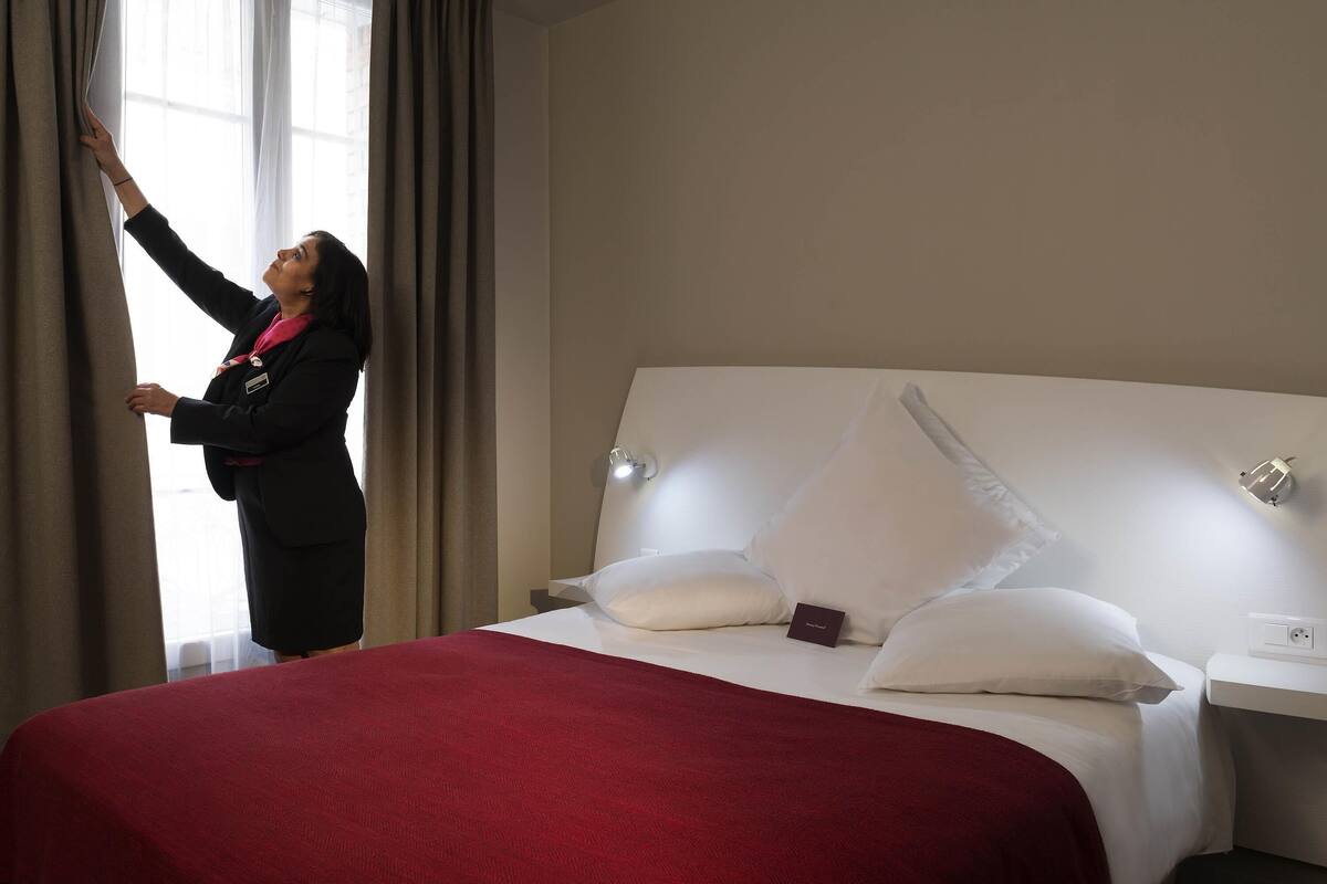 Een hotelkamer met een bed, nachtkastje, lamp en raam met gordijnen.