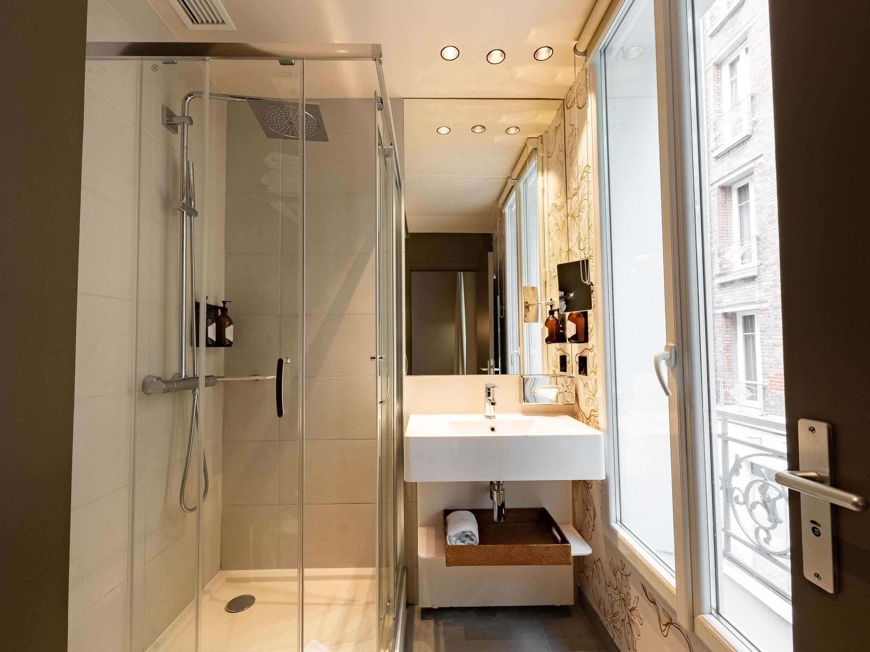 Ein modernes Badezimmer mit einer gläsernen Dusche, einem weißen Waschbecken und einem Fenster mit Blick ins Freie.