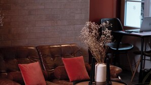 A cozy seating area with a brown leather sofa and chairs, a small round table with a vase of dried flowers, and a laptop on a desk. - Mercure Paris Levallois Perret (Levallois-Perret)