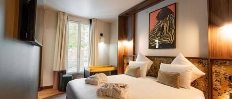A hotel room with a large bed, a desk, a chair, a TV, and a window with curtains.