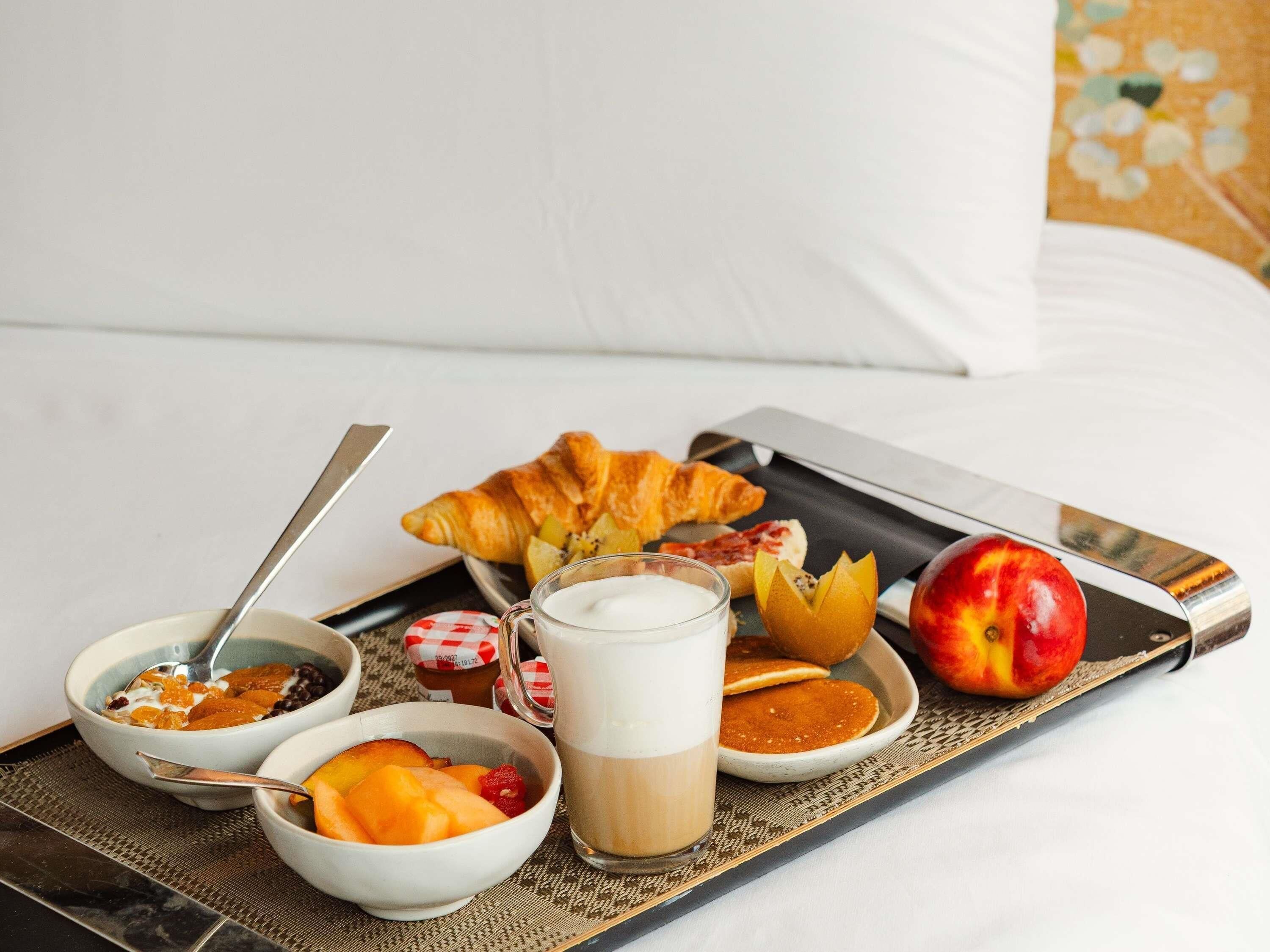 A breakfast tray with croissants, fruit, yogurt, and a glass of milk on a bed.