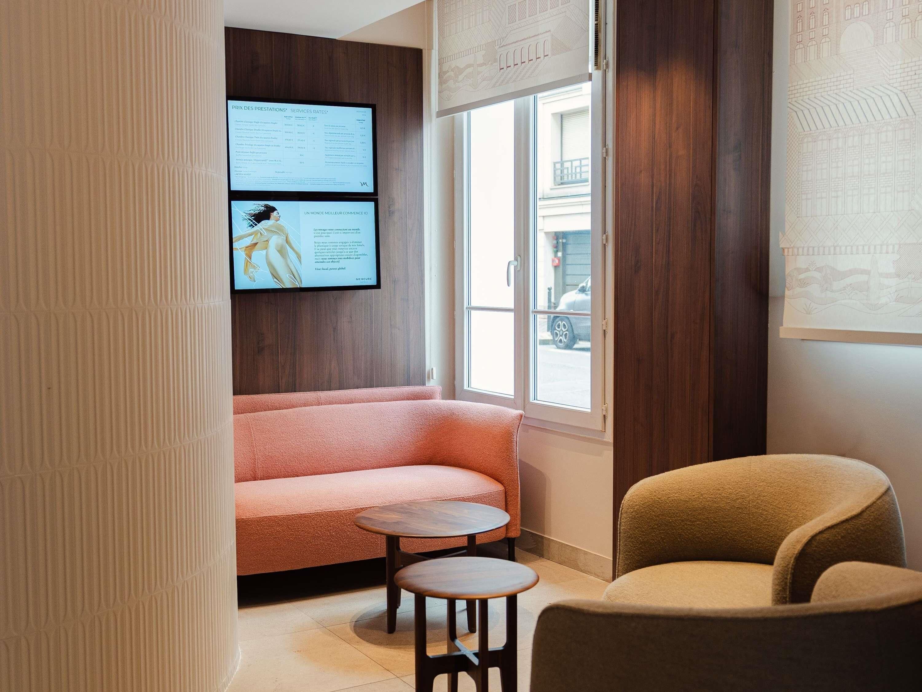 A room with a sofa, a chair, a small table, and a wall-mounted screen displaying text.