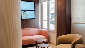 A room with a sofa, a chair, a small table, and a wall-mounted screen displaying text.