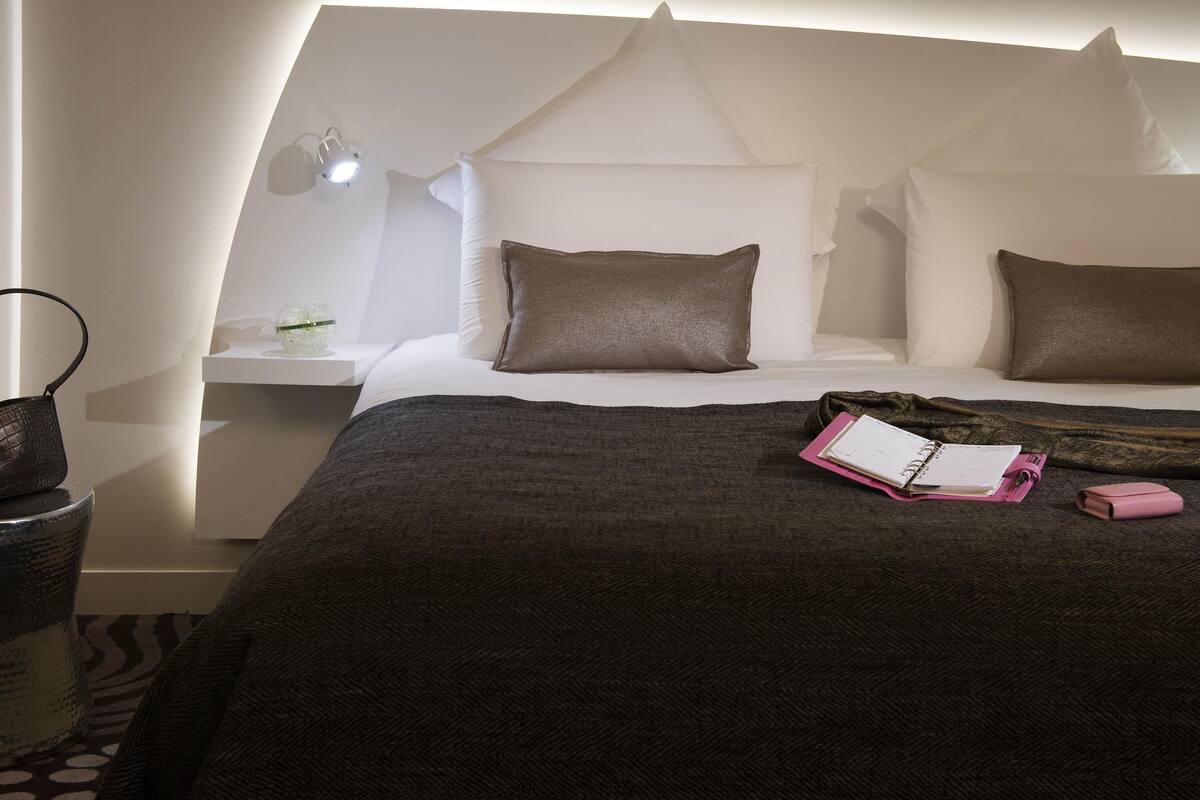 Een verzorgde hotelkamer met een bed, nachtkastje, lamp en een klein tafeltje met een glazen vaas.