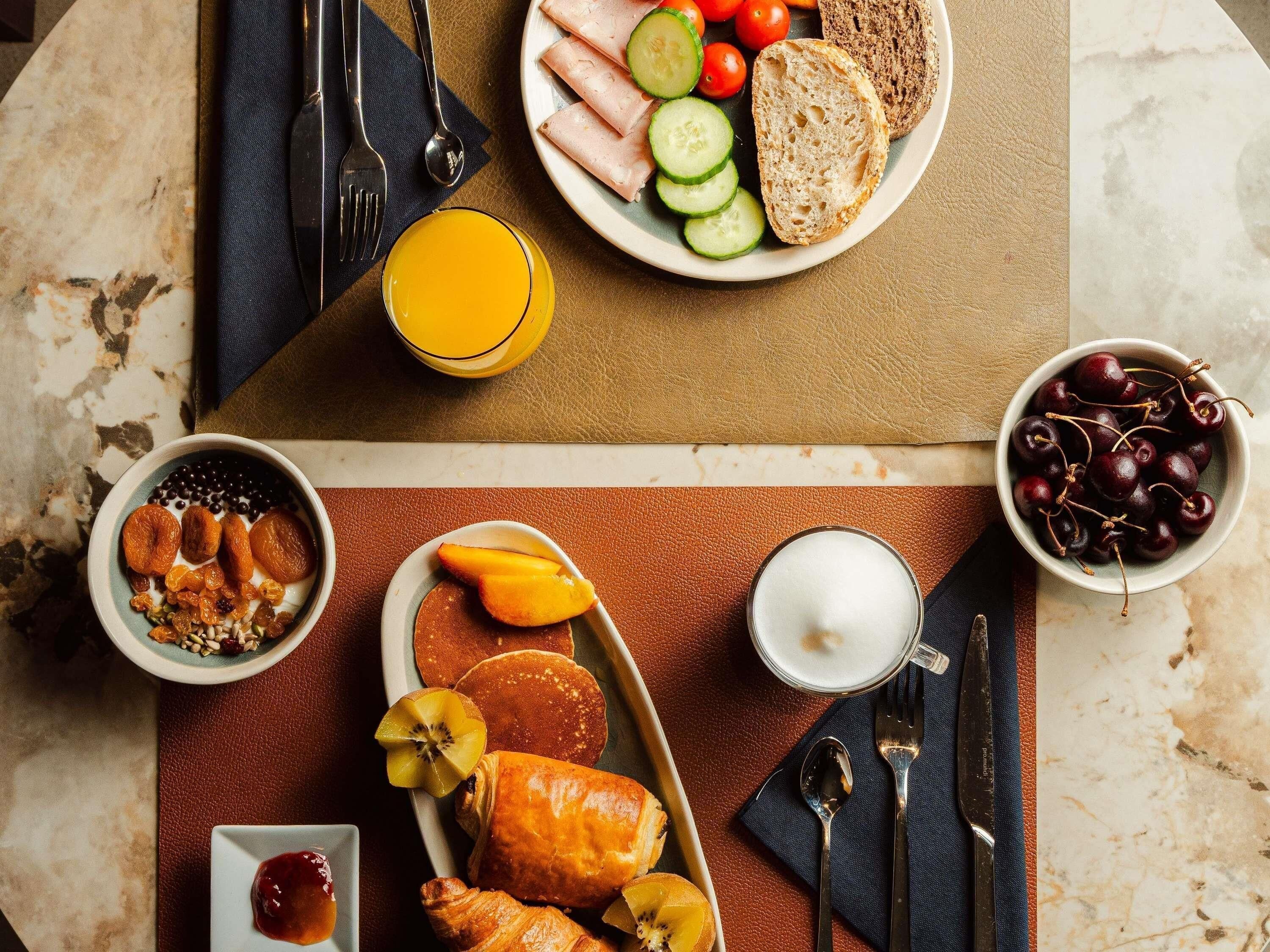 A breakfast setting with a plate of sliced bread, tomatoes, cucumbers, and a bowl of cherries.