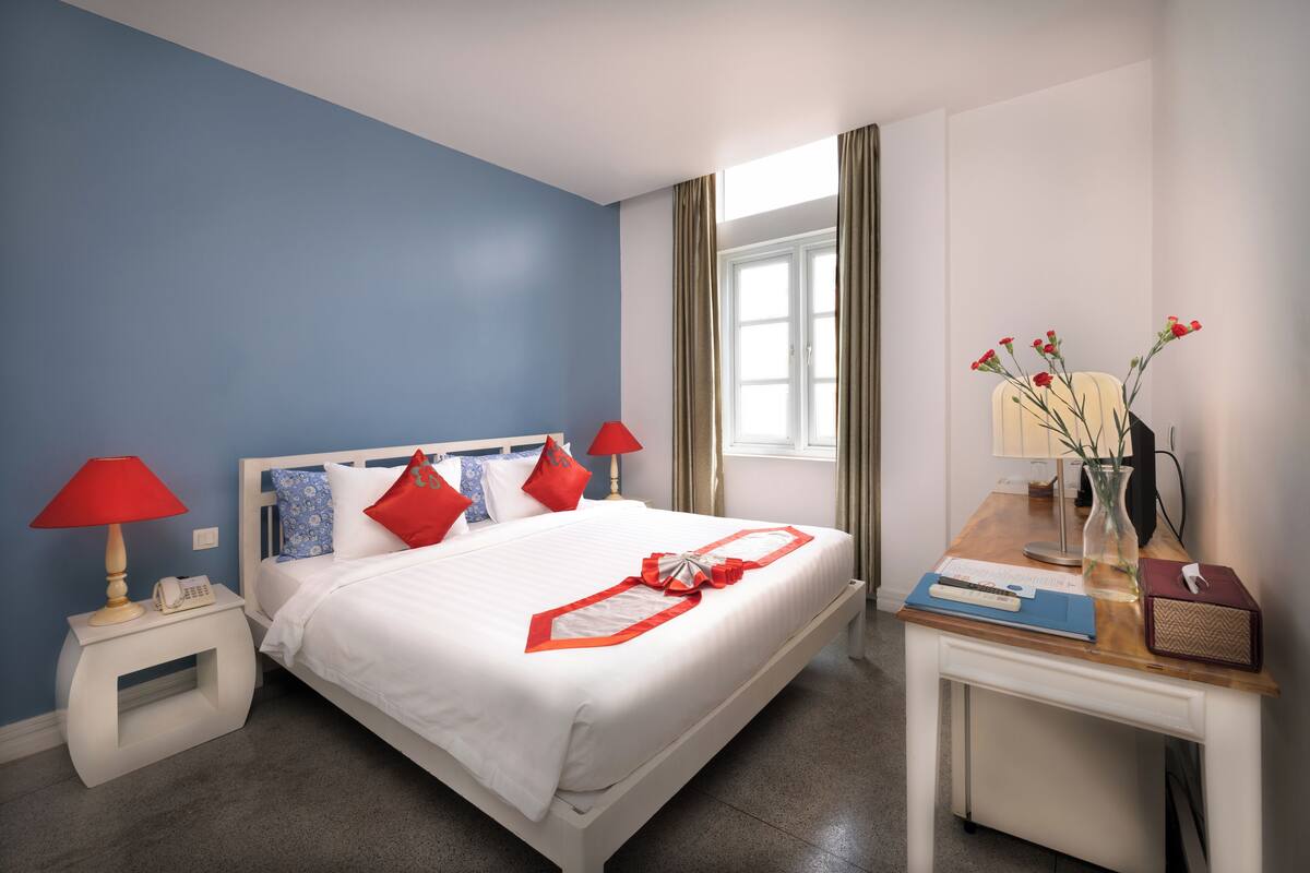 Ein Hotelzimmer mit Bett, Nachttisch, Schreibtisch und Fenster.