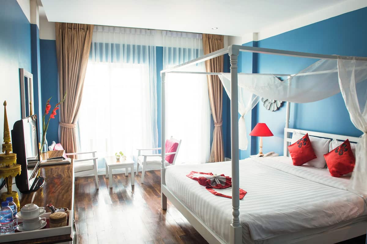 Ein Bett mit Himmel, ausgestattet mit weißer Bettwäsche und roten Kissen, ein Nachttisch mit Lampe sowie ein Sessel in einem Zimmer mit blauen Wänden und Holzboden.