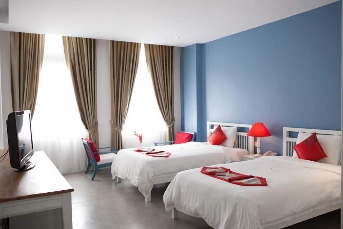 Ein Hotelzimmer mit zwei Betten, einem Schreibtisch, einem Fernseher und einem Fenster mit Vorhängen.