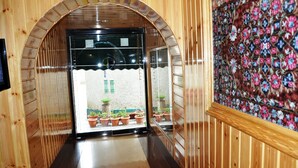 A wooden hallway with a tiled floor, a glass door leading outside, and a floral-patterned wall. - Hotel SADAF (Srinagar)