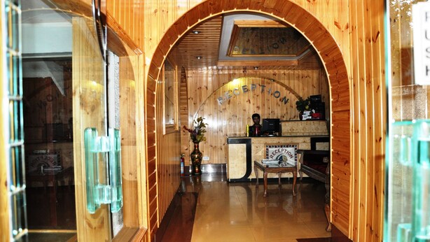 A reception area with a wooden archway, a reception desk, and a chair. - Hotel SADAF (Srinagar)