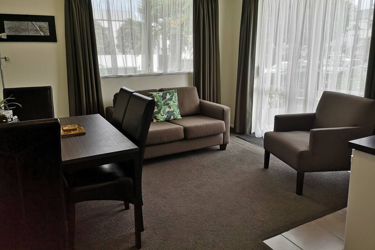 A living room with a sofa, a chair, a dining table, and a lamp.