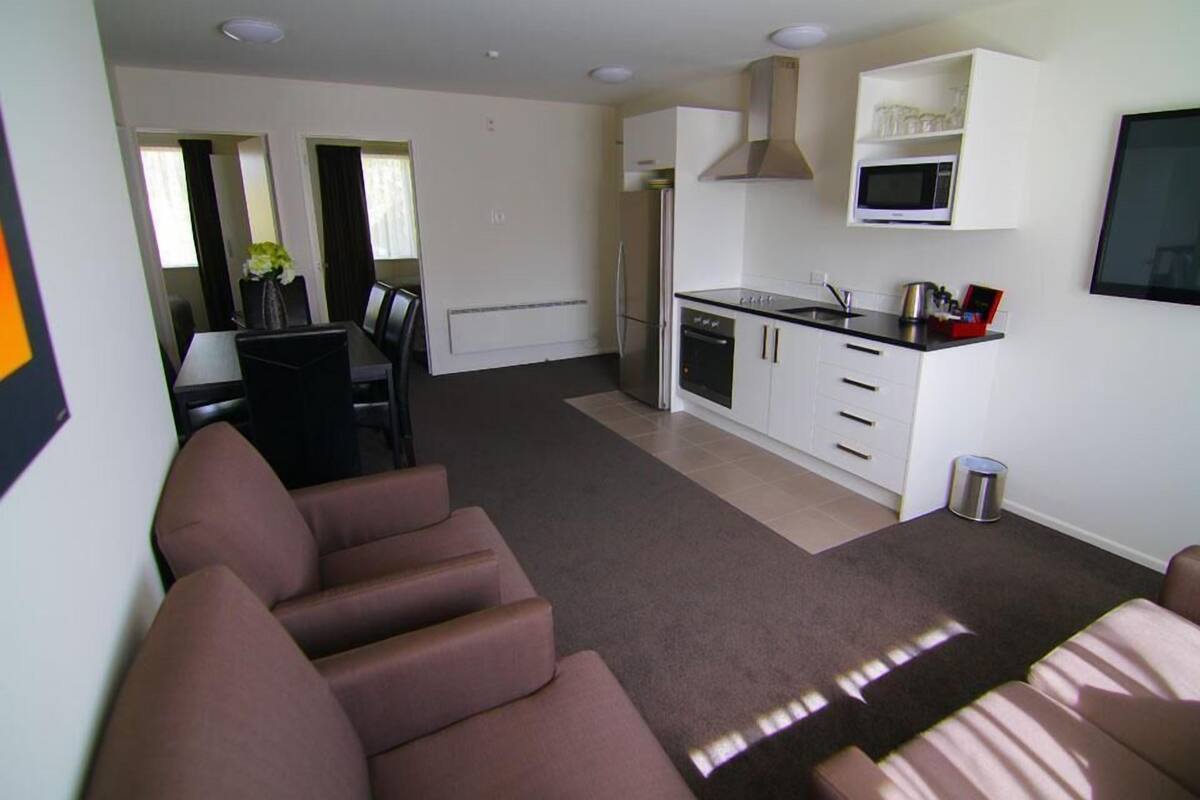 A modern living room with a sofa, a dining area with chairs, a kitchen with a microwave, and a small trash can.