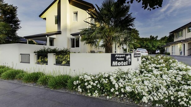 Een modern motel, met een bord waarop staat 'Airport Palms Motel'.