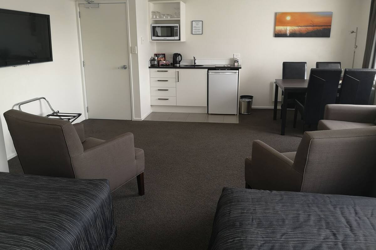A modern hotel room with a living area, kitchenette, and a dining table.