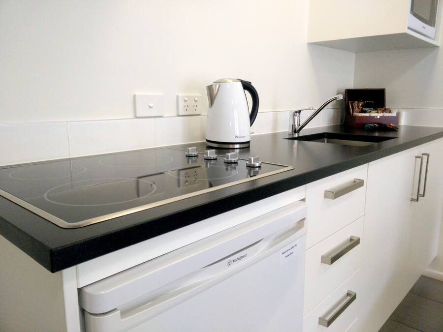 A kitchen with a black countertop, white cabinets, a built-in dishwasher, and a kettle.