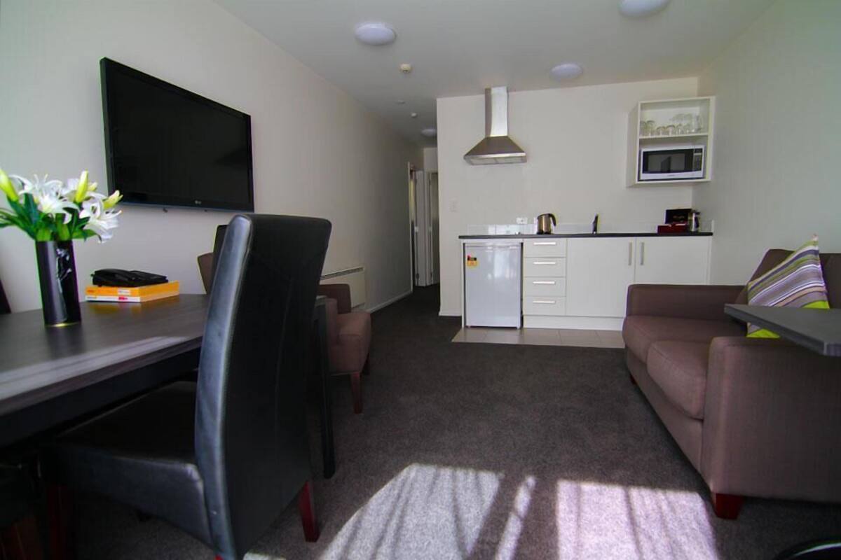 A modern living room with a flat-screen TV, a dining area with a table and chairs, a kitchen with a microwave, and a sofa with a striped pillow.