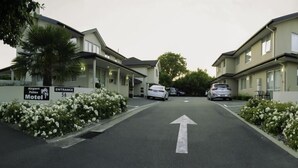 Straatbeeld van een motel met twee verdiepingen, een duidelijke richtingpijl op de weg en een bord dat de ingang van het Airport Palms Motel aangeeft.