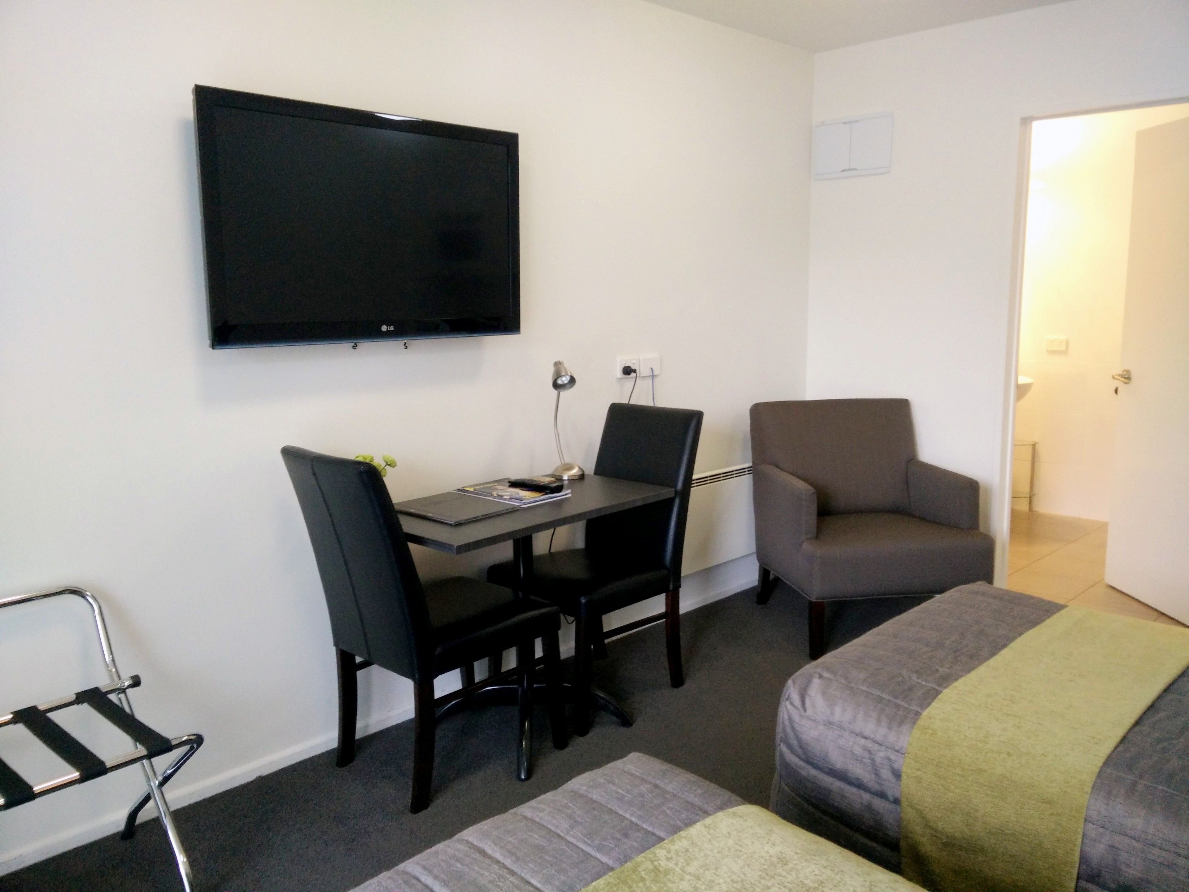 Una habitación de hotel pequeña con escritorio, dos sillas, televisor y cama.