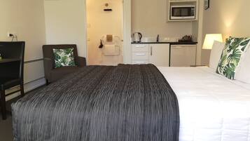 Una habitación de hotel con cama, escritorio, silla, microondas y una pequeña cocina americana.