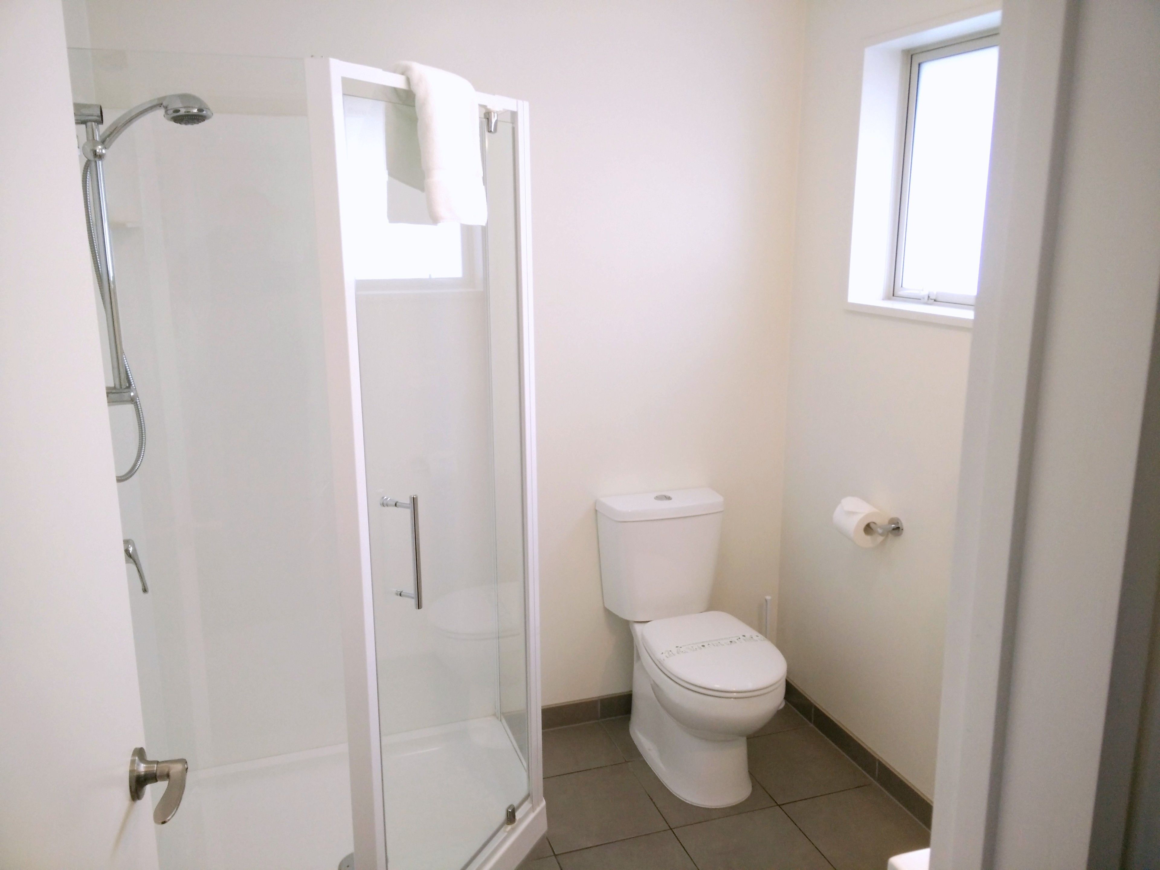 Un baño con ducha de vidrio, inodoro y ventana.