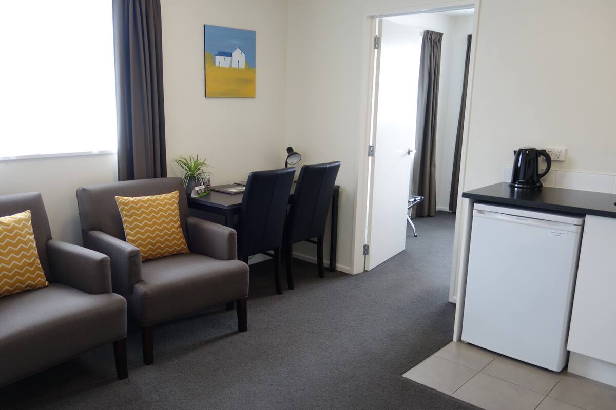 A room with two sofas, a dining table with chairs, a coffee maker, and a refrigerator.