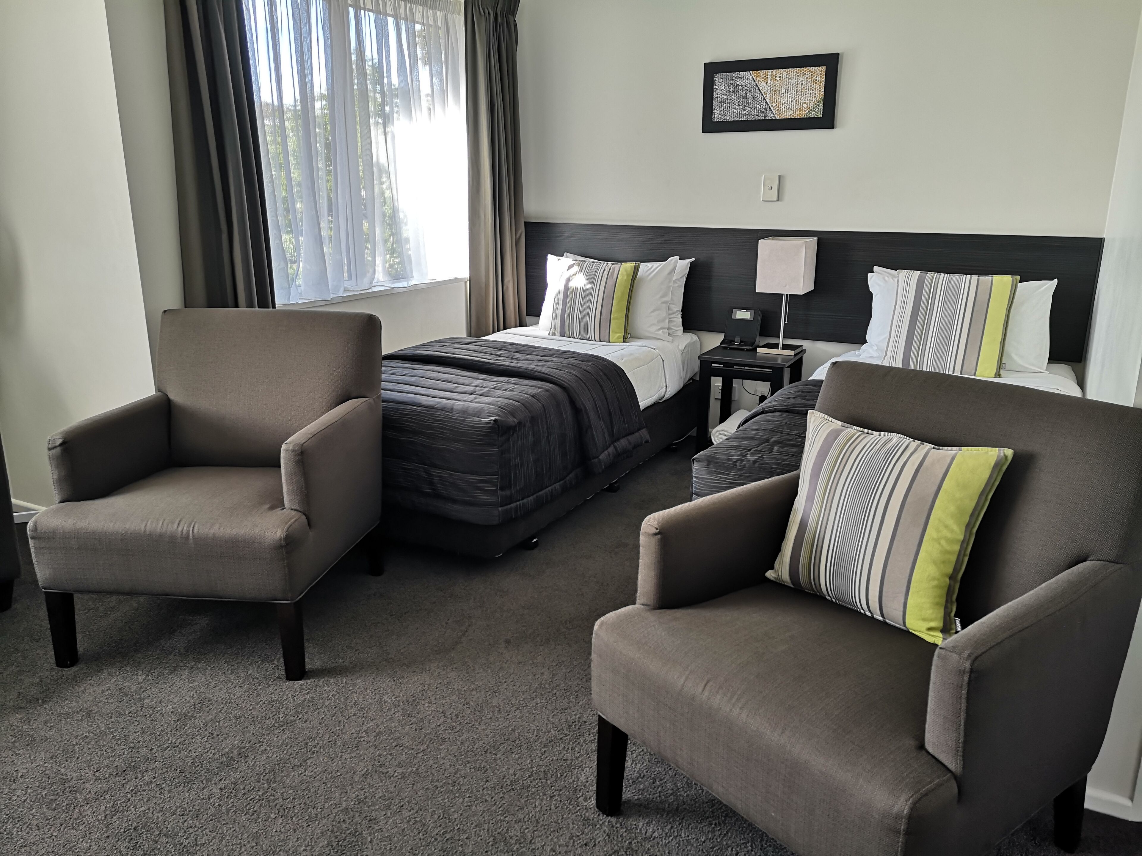 Une chambre d’hôtel avec un lit, deux fauteuils, une table de chevet et un tableau au mur.