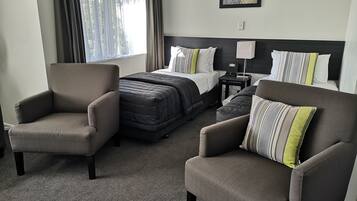 Une chambre d’hôtel avec un lit, deux fauteuils, une table de chevet et un tableau au mur.
