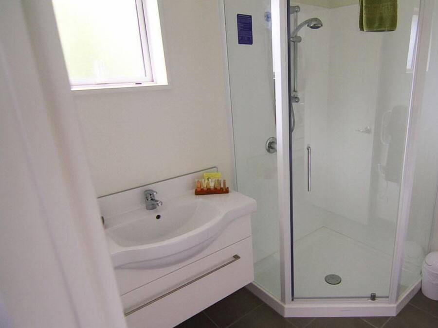 Un baño con lavamanos blanco, cabina de ducha de vidrio y un pequeño cubo de basura.
