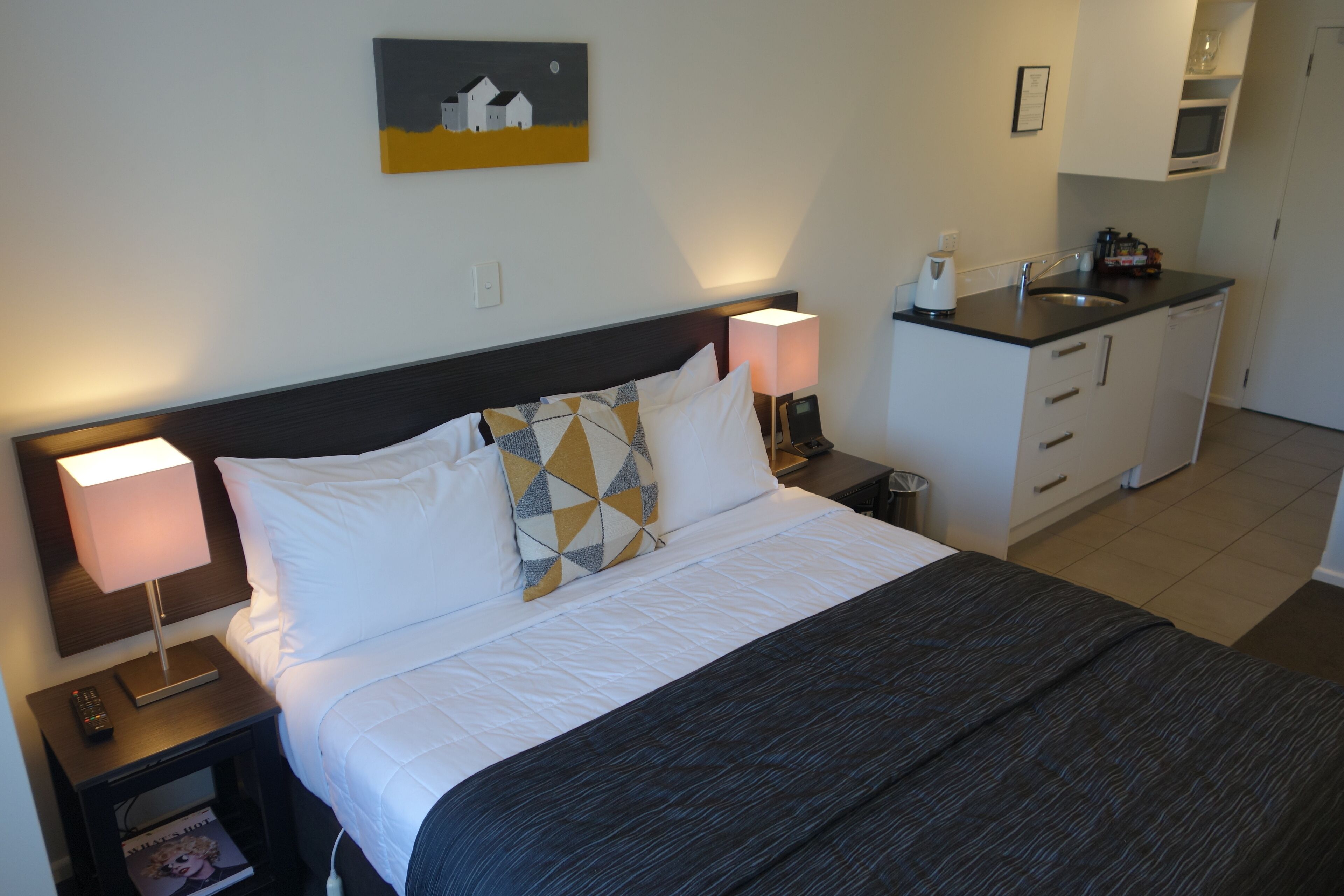 Ein Hotelzimmer mit Bett, Nachttisch, Lampe und einer kleinen Küchenzeile.