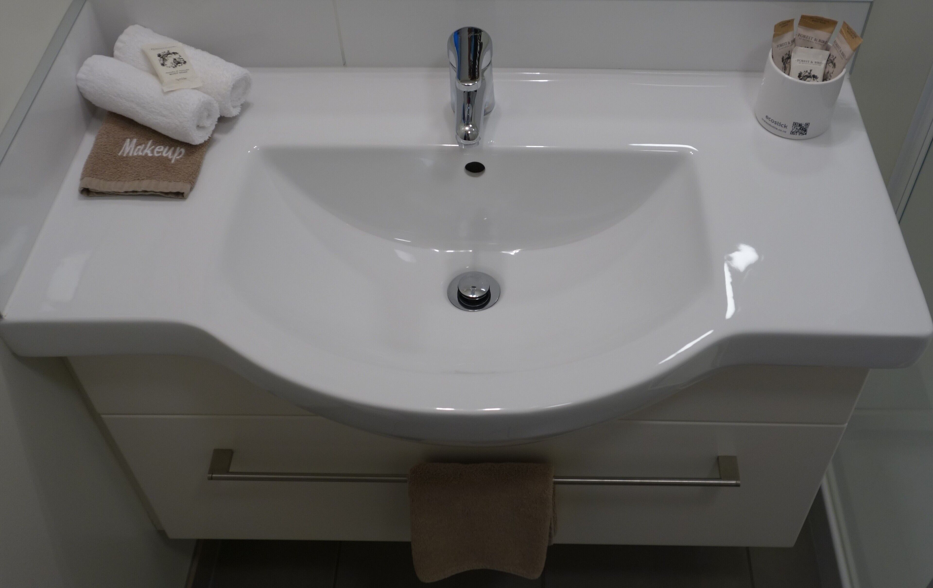 Un lavandino da bagno con una vasca bianca, un rubinetto cromato e un porta asciugamani con due asciugamani.