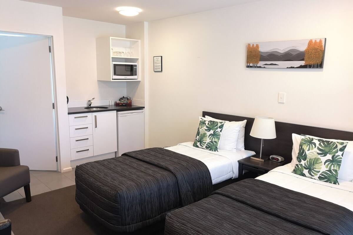 A hotel room with two beds, a kitchenette, and a painting on the wall.