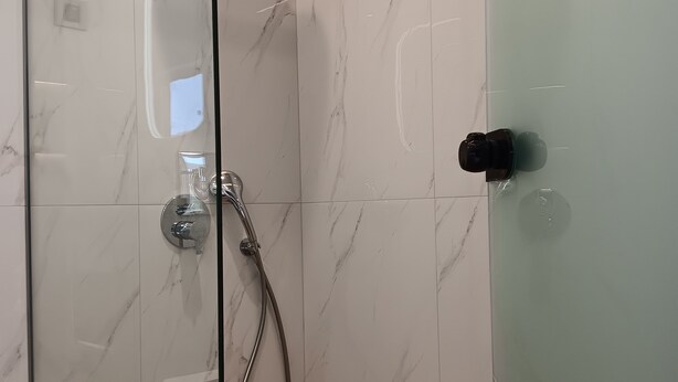 Una ducha envuelta en vidrio con un cabezal de ducha de mano y un grifo empotrado.