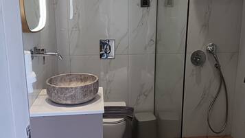 Ein modernes Badezimmer mit Marmorwand, einer Duschkabine aus Glas, einem weißen Waschbecken mit Steintonne und einer Toilette.