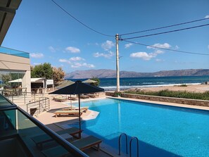 Piscina con sillones reclinables y sombrillas, con vistas a una playa y montañas.